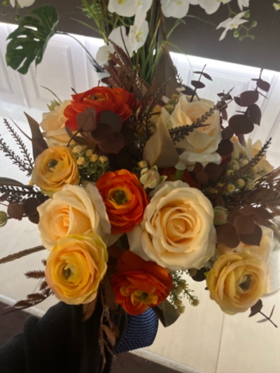 A wedding bouquet of faux flowers in creams and orange shades and enhanced with a selection of faux greens