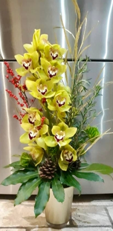 A beautiful fresh flower arrangement of fresh cymbidium orchid, and a selection of mixed foliages designed in a cylinder vase