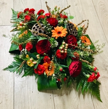 A stunning funeral or memory tribute, created with a selection of red and orange flowers and twig pieces approx 3 ft long