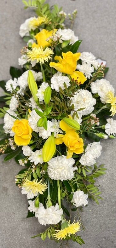 Beautiful sympathy tribute with yellow roses and a selection of white flowers and green foliage, very suitable for a funeral or a memory tribute